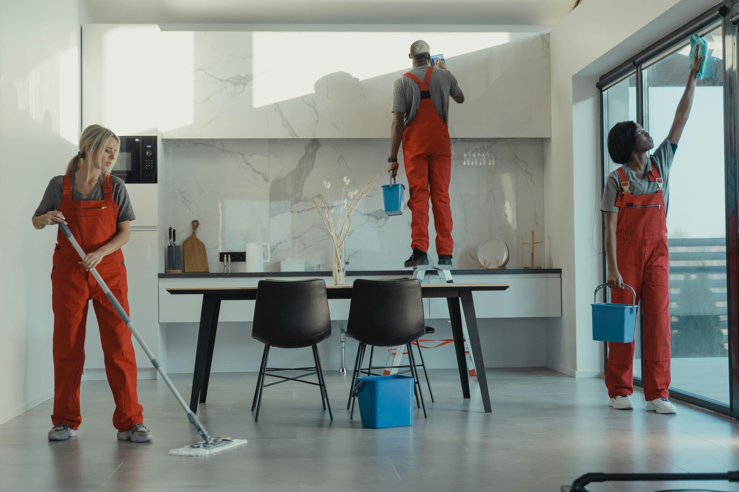 pexels-photo-6197108-6197108 Group of cleaners in red uniforms mopping and wiping glass in a modern dining room.