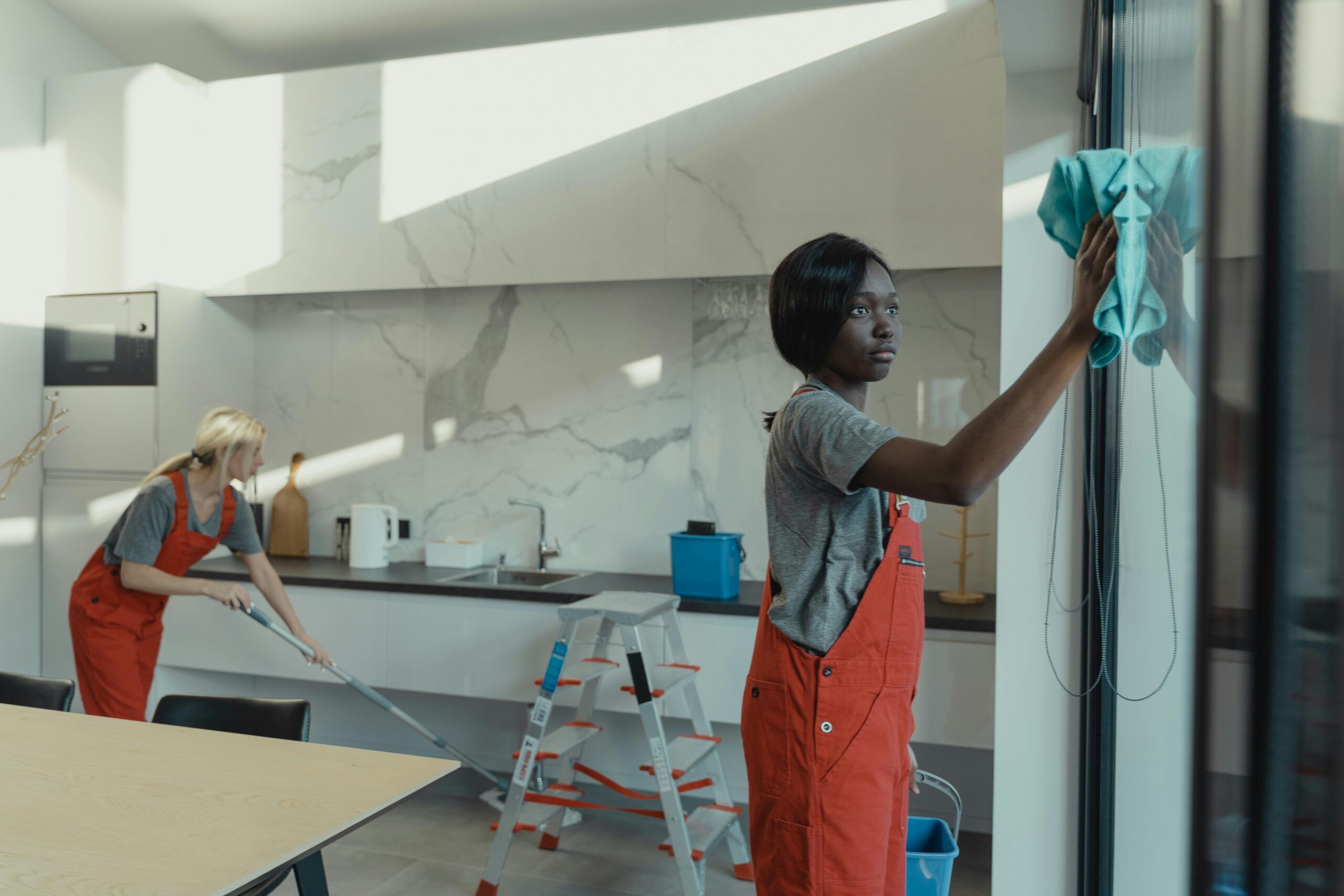 pexels-photo-6197121-6197121 Two women cleaning a modern kitchen, wiping glass surfaces and mopping the floor.